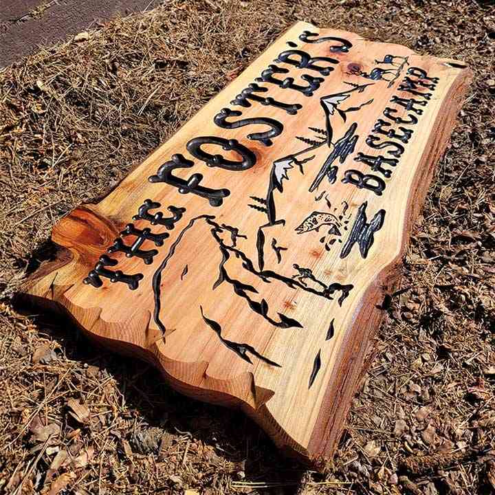 Hand-carved custom cabin sign with 'The Foster's Basecamp' text, featuring mountain and wildlife artwork on rustic live-edge wood.