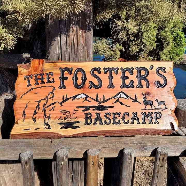 Hand-carved custom cabin sign with 'The Foster's Basecamp' text, featuring mountain and wildlife artwork on rustic live-edge wood.